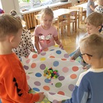 dzieci unoszą na papierowym obrusie kolorowe kulki.jpg