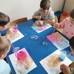 Dzieci dmuchają słomką w słoiczek z kolorową wodą.