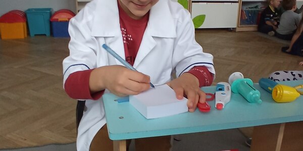chłopiec w faruchu lekarskim pisze po kartce.jpg