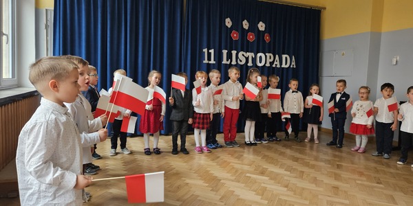 grupa dzieci z flagami w rękach stojących w półkolu podczas występów z okazji dnia niepodległości.jpg
