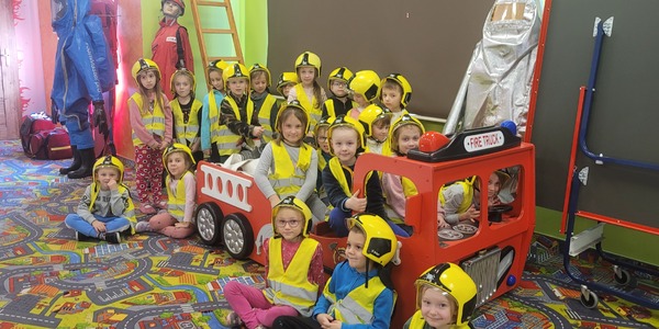 grupa dzieci pozuje do zdjęcia siedząc w zabawkowym modelu wozu strażackiego.jpg
