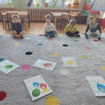 dzieci siedzą na dywanie, przyglądają się ilustracjom z balonami