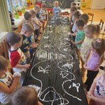 dzieci stoją przed stolikami z czarną folią i białą farbą