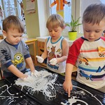 dzieci malują rączkami białą farbą po czarnej folii 