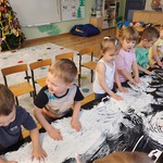 dzieci malują rączkami białą farbą po czarnej folii 
