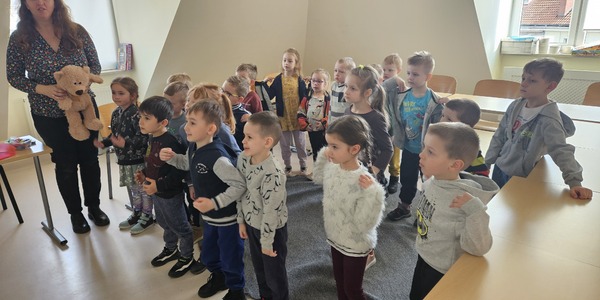 dzieci stoją przed tablicą multimedialną i naśladują ruch do piosenki.jpg