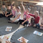 Dzieci siedzą na dywanie wokół ilustracji z misiem.jpg