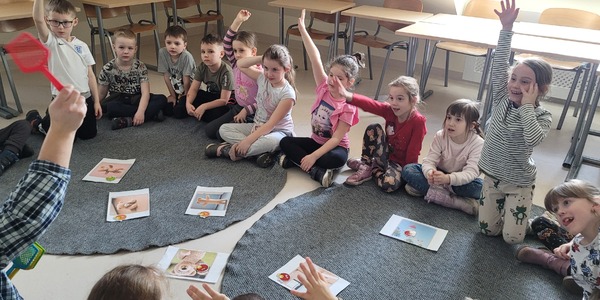 Dzieci siedzą na dywanie wokół ilustracji z misiem.jpg